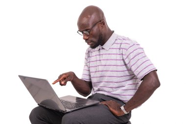 Optik gözlüklü genç adam sandalyede oturuyor, çalışıyor ve dizüstü bilgisayarını işaret ediyor..