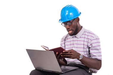 Genç mühendis kasketli, sandalyede oturmuş dizüstü bilgisayarla notları kontrol ediyor..