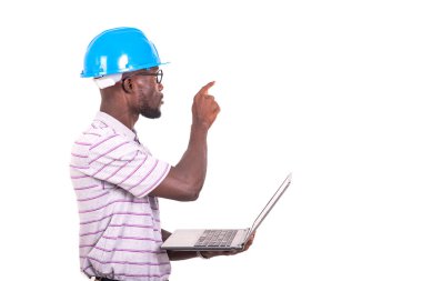 Genç mühendis mavi güvenlik kaskı takıyor, dizüstü bilgisayarı tutuyor ve parmağıyla gözüne işaret ediyor..