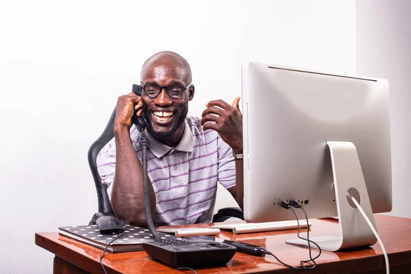 young business man sitting at the desk facing the laptop and talking on mobile phone while smiling.