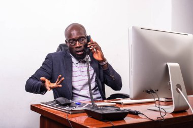 Genç iş adamı dizüstü bilgisayar karşısında oturuyor ve cep telefonuyla konuşuyor..