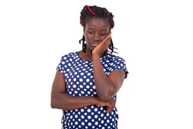 Beyaz noktalı mavi elbiseli düşünceli genç bir kadın. Başı öne eğik ve ilgisiz bir şekilde yan bakıyor. Beyaz arka planda duruyor..