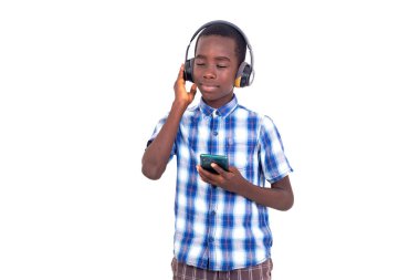 Kareli tişörtlü genç beyaz arka planda durup müzik dinlerken cep telefonu ve kulaklıkla gülümsüyor..