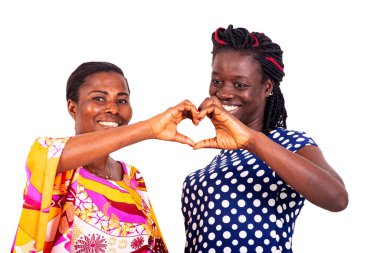 İki güzel kadın gülümserken kalp şeklini parmaklarıyla gösteriyor..