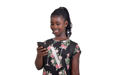 Sırt çantası takan genç bir kız öğrenci beyaz arka planda duruyor ve cep telefonuyla gülümsüyor.