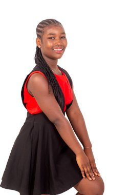 Kırmızı ve siyah elbiseli güzel bir kız beyaz bir arka planda duruyor elleri dizlerinin üstünde kameraya bakıp gülümsüyor..