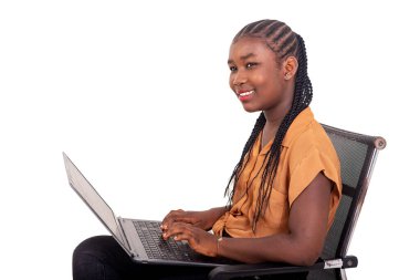 Pantolon giymiş genç bir bayan öğrenci sandalyede oturmuş dizüstü bilgisayarla gülümsüyor..