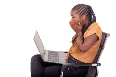 Pantolon giymiş genç bir bayan öğrenci evde oturmuş dizüstü bilgisayarla çalışıyor. Şaşırmış görünüyor..