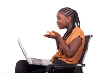 Pantolon giymiş genç bir kız çocuğu koltukta oturmuş dizüstü bilgisayarla video görüşmesi yapıyor..