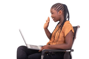 Pantolon giymiş genç bir kız çocuğu koltukta oturmuş dizüstü bilgisayarla video görüşmesi yapıyor..