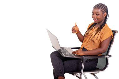 Pantolon giymiş genç bir bayan öğrenci evinde oturmuş dizüstü bilgisayarla video görüşmesi yapıyor ve gülümsüyor..