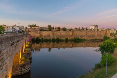 İspanya 'nın Merida kentindeki Alcazaba kalesine giden Guadiana nehri üzerindeki Roma köprüsünün günbatımı manzarası
