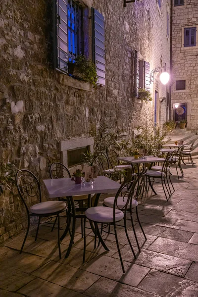 Hırvatistan 'ın eski Sibenik kentinde dar bir sokaktaki restoran masalarının gece manzarası