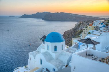 Yunanistan 'ın Santorini kentindeki Oia kasabasının günbatımı ve mavi kupa manzarası