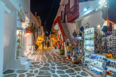 Mykonos, Yunanistan, 26 Eylül 2020: Yunanistan 'ın eski Mykonos kentindeki dar bir sokaktaki turist dükkanlarının gece manzarası