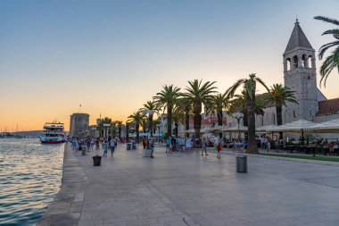 Trogir, Hırvatistan, 22 Temmuz 2020: Hırvatistan 'ın Trogir kentinde insanlar gün batımında deniz kenarında geziniyorlar