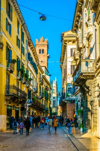 VERONA, ITALY, 19 Mart 2016: İnsanlar Verona, İtalya 'daki Piazza delle erbe' ye doğru dar bir sokakta geziniyor