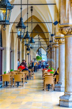 KRAKOW, POLAND, 11 AĞUSTOS 2016: Polonya 'nın Krakow / Krakow kentindeki sukiennice pazar yerinin kemerlerinin altında insanlar öğle yemeği yiyorlar.