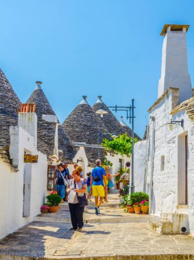 ALBEROBELLO, İtalya, 21 Haziran 2014: Turistler Alberobello, İtalya 'daki trulli evler arasında güneşli bir günün tadını çıkarıyorlar.