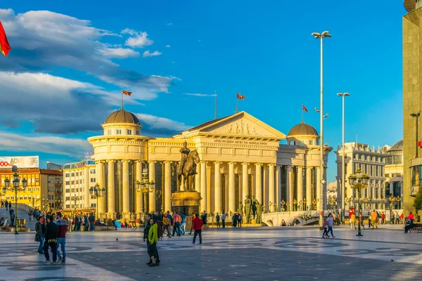 ÜSKÜP, MACEDONIA, 14 Mayıs 2016: Arka planda Macar arkeoloji müzesi bulunan Skopje 'deki Macedonia Meydanı' ndan insanlar geçiyor.