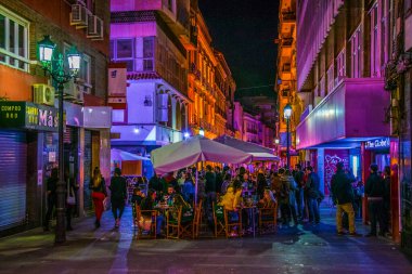 ALICANTE, İspanya, 2 HAZİRAN 2016: İspanya 'nın tarihi kenti Cezayir' de yerel halkın pek çok barın önünde gece hayatının tadını çıkardığı dar bir caddenin görüntüsü.