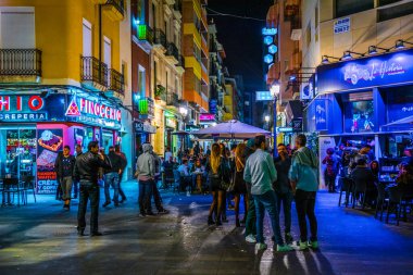 ALICANTE, İspanya, 2 HAZİRAN 2016: İspanya 'nın tarihi kenti Cezayir' de yerel halkın pek çok barın önünde gece hayatının tadını çıkardığı dar bir caddenin görüntüsü.