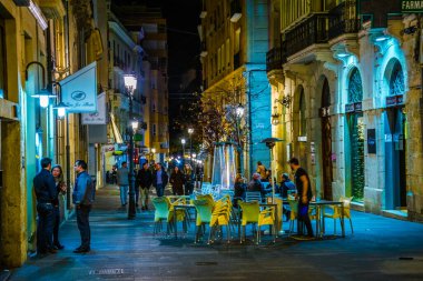 ALICANTE, İspanya, 2 HAZİRAN 2016: İspanya 'nın tarihi kenti Cezayir' de yerel halkın pek çok barın önünde gece hayatının tadını çıkardığı dar bir caddenin görüntüsü.