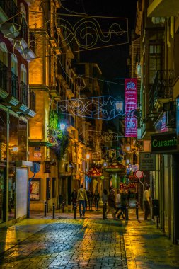 ALICANTE, SPAIN, JANUARY 2, 2016: View of a narrow street in the historical center of spanish city alicante where local people enjoy nightlife in front of many bars.