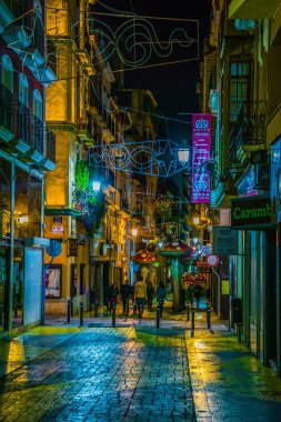 ALICANTE, SPAIN, JANUARY 2, 2016: View of a narrow street in the historical center of spanish city alicante where local people enjoy nightlife in front of many bars.