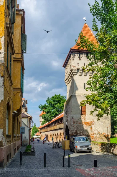 SIBIU, ROMANIA, 6 HAZİRAN 2015: Ortaçağ savunma duvarı ve Transilvanya 'nın Transilvanya bölgesindeki Marangoz Kulesi boyunca dolaşan kimliği belirsiz kişiler.