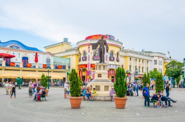 VIENNA, AUSTRIA, HAZİRAN 2016: İnsanlar Avusturya 'nın Viyana kentindeki Prater Lunaparkı' nın ana girişinin yanındaki bir sihirbazın heykeli altında dinleniyor.