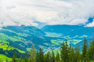 Avusturya 'daki Krimmml şelalesinin yanında bulutlarla kaplı yeşil bir vadi manzarası.