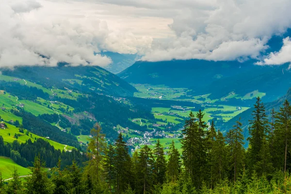 Avusturya 'daki Krimmml şelalesinin yanında bulutlarla kaplı yeşil bir vadi manzarası.