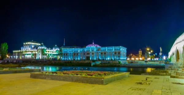 Ünlü taş köprünün arkasındaki Skopje 'deki ulusal tiyatronun gece manzarası