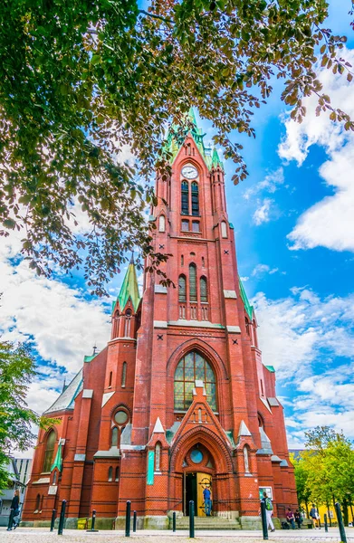 People are passing by red Johanneskirken church in the norwegian city Bergen