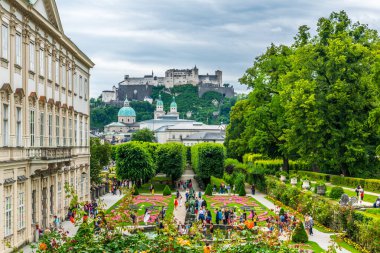 People are strolling through Mirabell Gardens with the old historic Fortress Hohensalzburg in the background in Salzburg, Austri