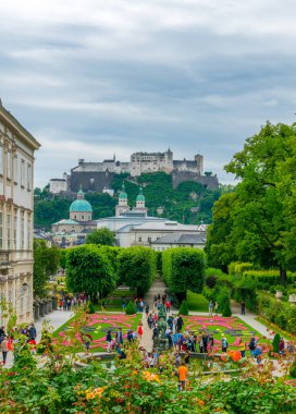 İnsanlar Mirabell Gardens 'ta eski tarihi Hohensalzburg Kalesi' nin arka planında geziniyorlar.