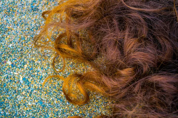 curly ginger hair on sand