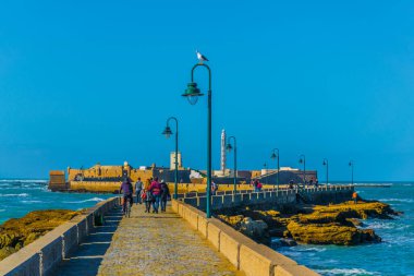 İnsanlar İspanya 'nın Cadiz kentindeki San Sebastian şatosuna giden dar bir tuğla yoldan geçiyorlar.