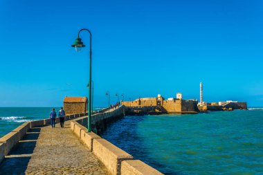 İnsanlar İspanya 'nın Cadiz kentindeki San Sebastian şatosuna giden dar bir tuğla yoldan geçiyorlar.