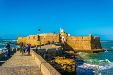 İnsanlar İspanya 'nın Cadiz kentindeki San Sebastian şatosuna giden dar bir tuğla yoldan geçiyorlar.