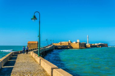 İnsanlar İspanya 'nın Cadiz kentindeki San Sebastian şatosuna giden dar bir tuğla yoldan geçiyorlar.
