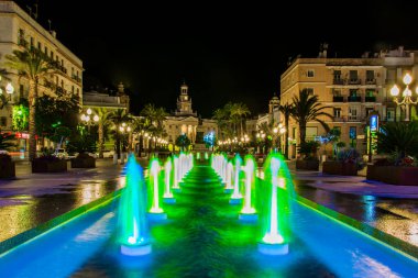 night view of a fountain situated on the square of saint john of god in cadiz with town hall on background