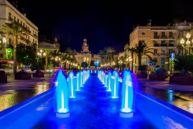 night view of a fountain situated on the square of saint john of god in cadiz with town hall on background