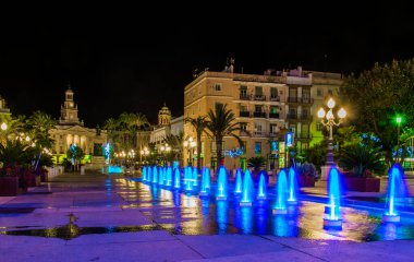 night view of a fountain situated on the square of saint john of god in cadiz with town hall on background