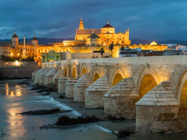 İspanyol şehri Cordoba 'daki La mezquita katedrali ile Guadalquivir nehri üzerindeki aydınlık Roma köprüsünün gece manzarası.