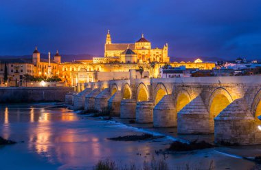 İspanyol şehri Cordoba 'daki La mezquita katedrali ile Guadalquivir nehri üzerindeki aydınlık Roma köprüsünün gece manzarası.