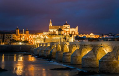 İspanyol şehri Cordoba 'daki La mezquita katedrali ile Guadalquivir nehri üzerindeki aydınlık Roma köprüsünün gece manzarası.