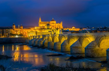 İspanyol şehri Cordoba 'daki La mezquita katedrali ile Guadalquivir nehri üzerindeki aydınlık Roma köprüsünün gece manzarası.