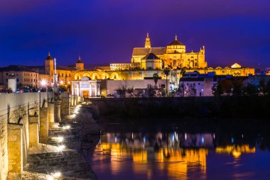 İspanyol şehri Cordoba 'daki La mezquita katedrali ile Guadalquivir nehri üzerindeki aydınlık Roma köprüsünün gece manzarası.